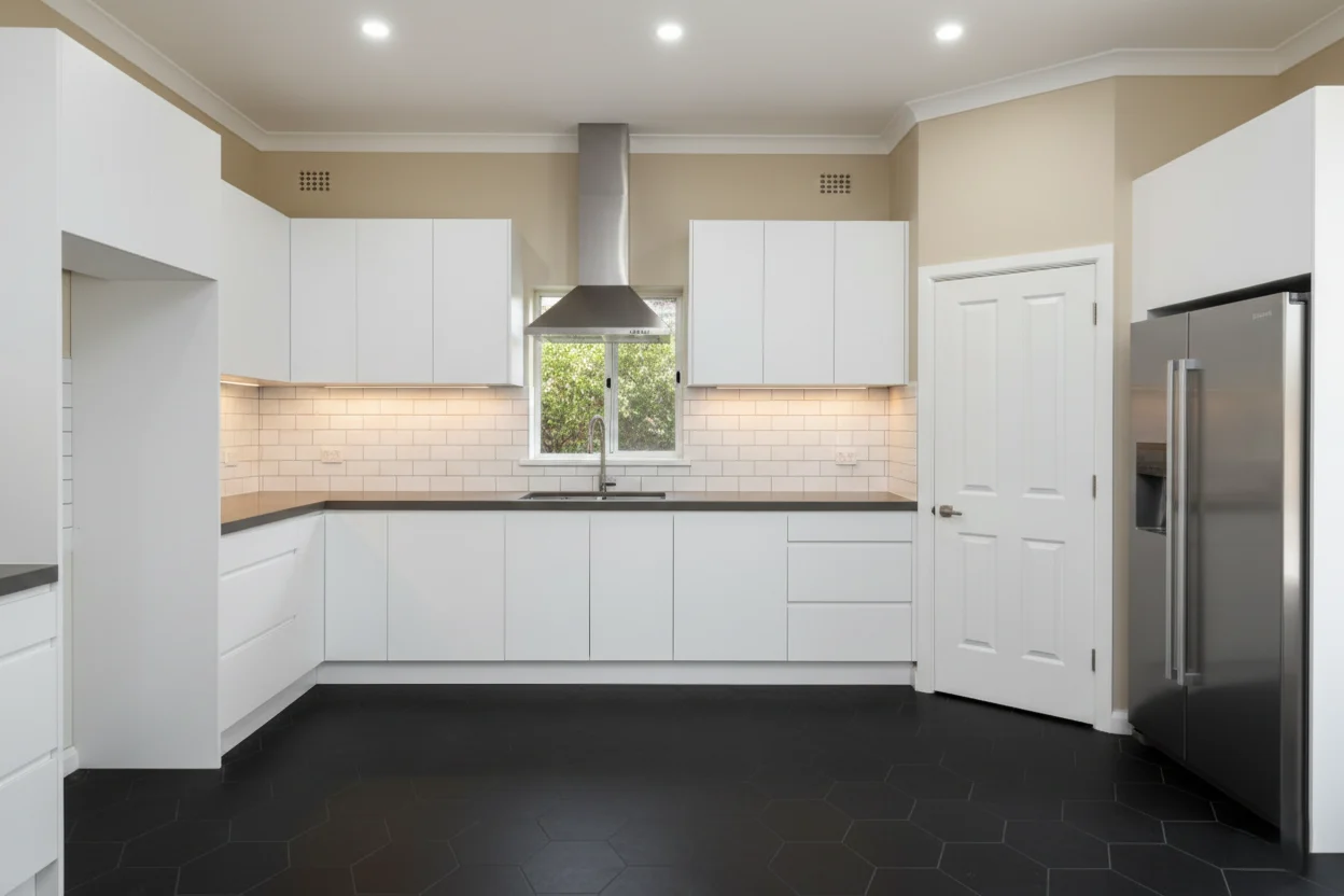 Modern white kitchen remodeling by Dream Space Remodeling featuring black hexagon tile flooring and white subway tile backsplash.
