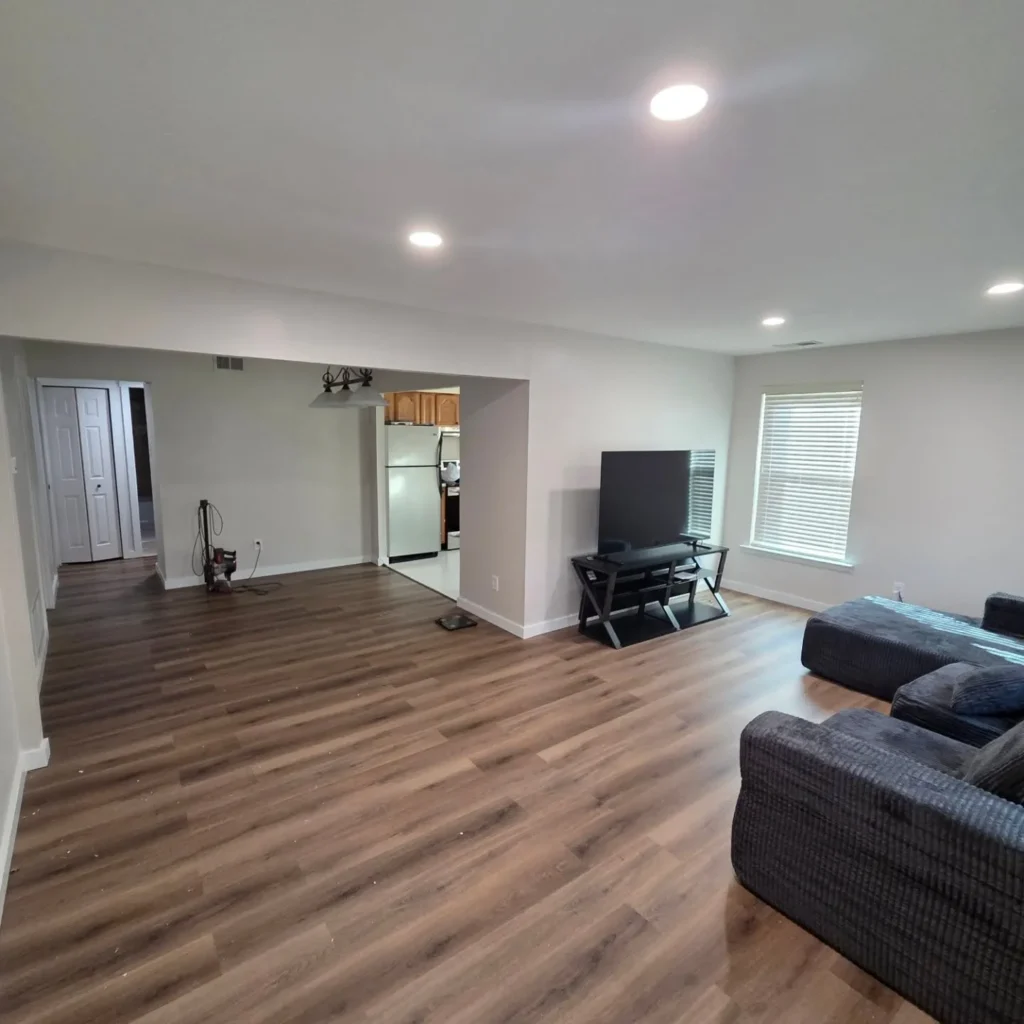 Modern open-concept finished basement by Dream Space Remodeling featuring dark wood flooring, recessed lighting, and a spacious living area.