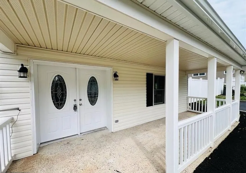 A clean and classic front porch renovation by Dream Space Remodeling featuring white double doors with decorative oval glass, white vinyl siding, matching support pillars, and a white safety railing.