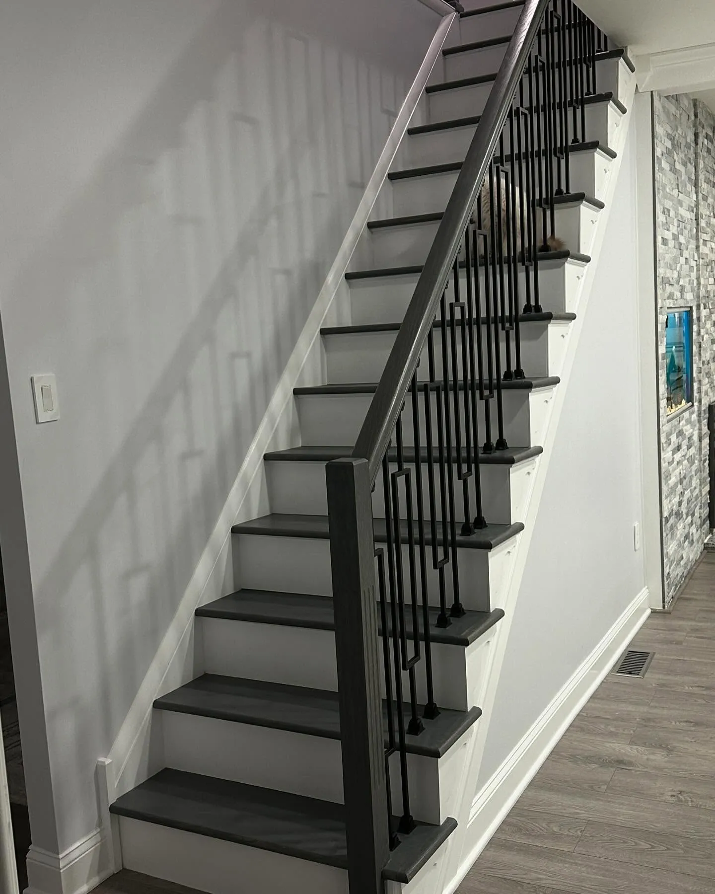 Modern staircase renovation by Dream Space Remodeling featuring dark gray treads and a custom black geometric metal railing.
